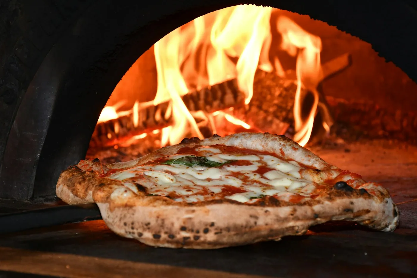 Pizza im Holzofen, dahinter Flammen