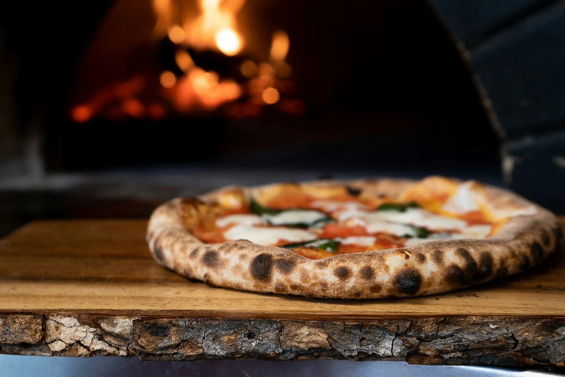 Neapolitanische Pizza auf einem Holzbrett vor dem brennenden Ofen